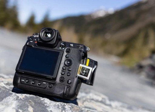Professional DSLR camera on a rock with an Exascend Essential CFexpress Type B card partially inserted in the memory card slot, outdoor mountain background blurred.