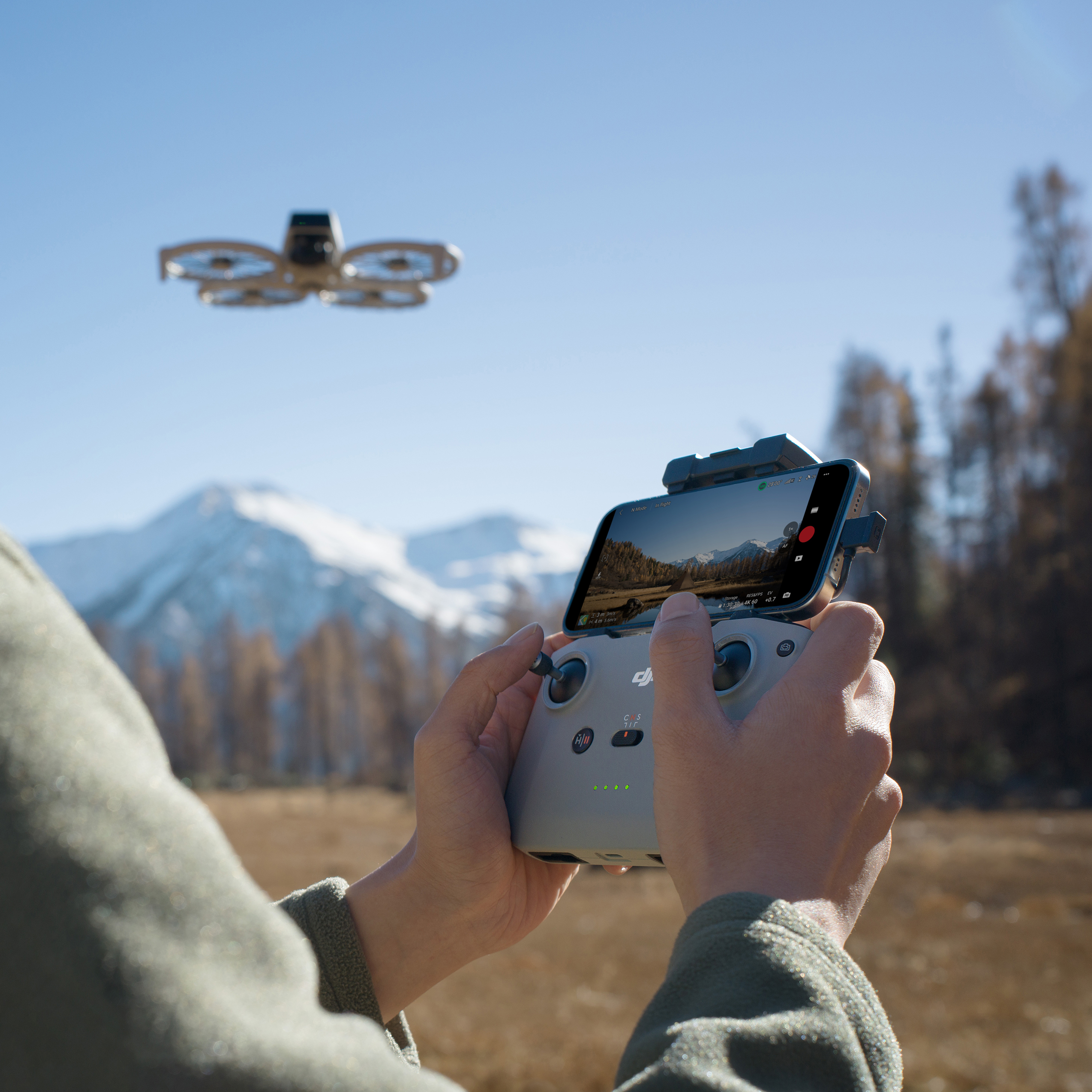 A DJI flip drone behing operated. A person's hands seen holding the remote in the foregraond and mountains in the background. 