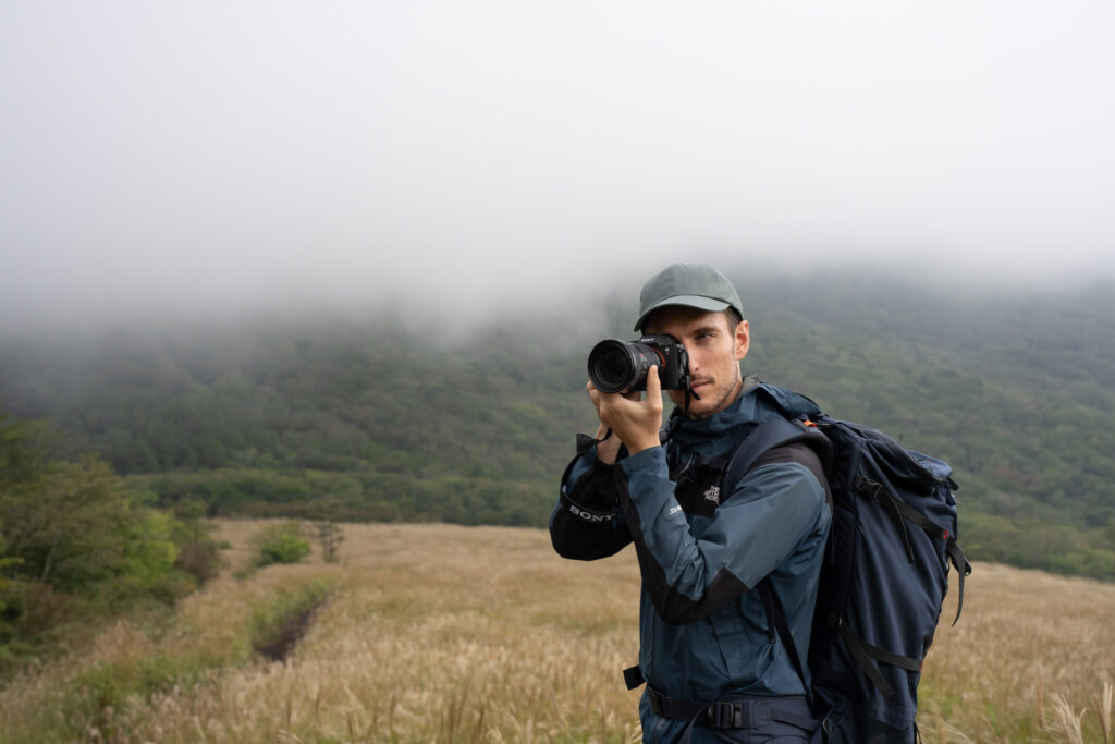 A man with a sony camera standing in a field heavy fog hangs over him.