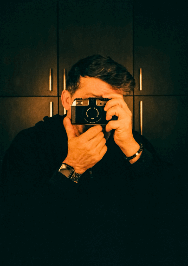 An image of aman holding a camera pointed toward the viewer. 